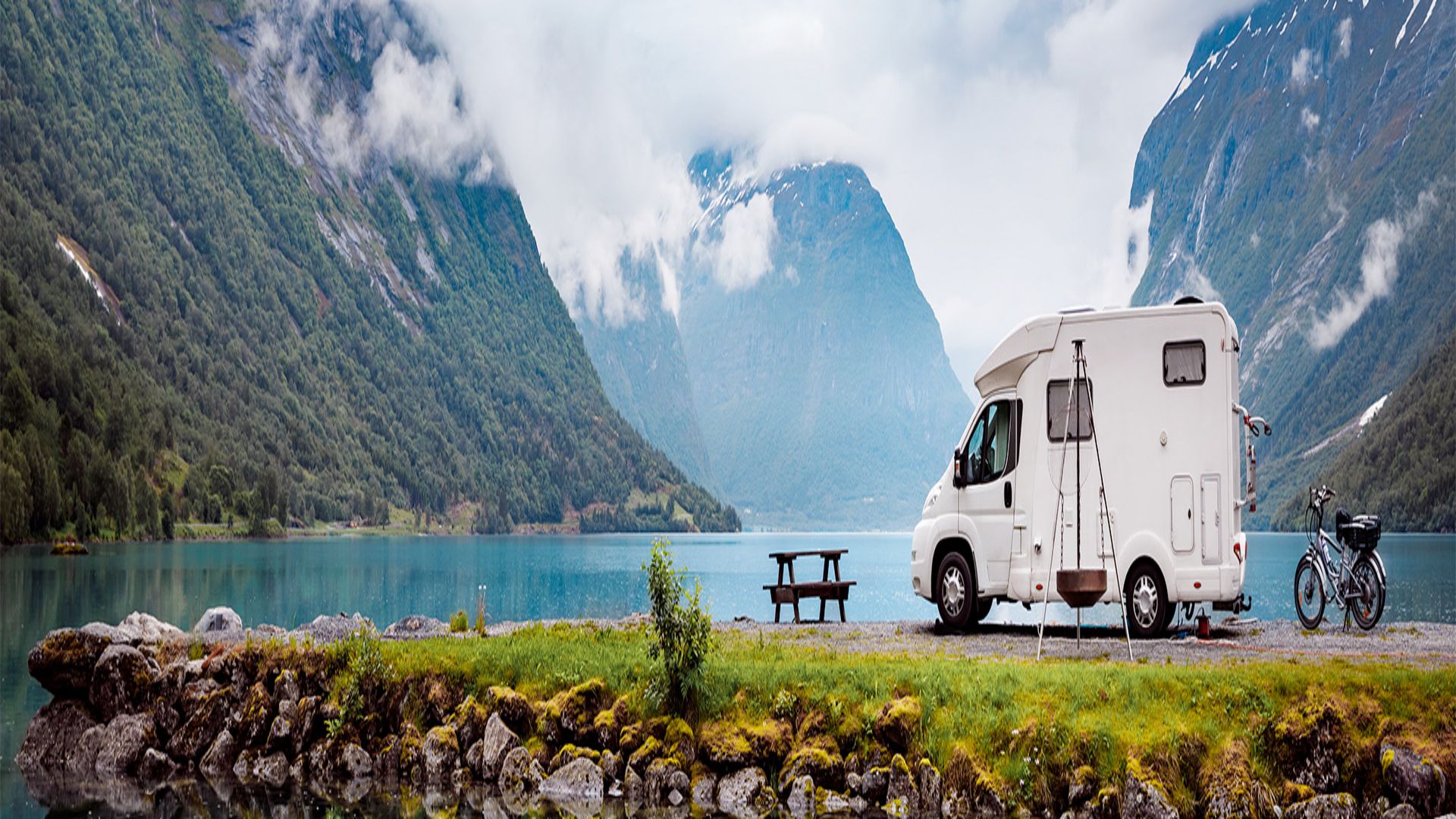 Wei&szlig;es Wohnmobil vor einem t&uuml;rkisenen See mit Bergen im Hintergrund